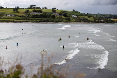 Temmuz 27th, 2019, Clonakilty, İrlanda-insanlar sörf, yüzme ve yüzme ile bir bulutlu gününde Inchydoney plajının panoramik görünümü