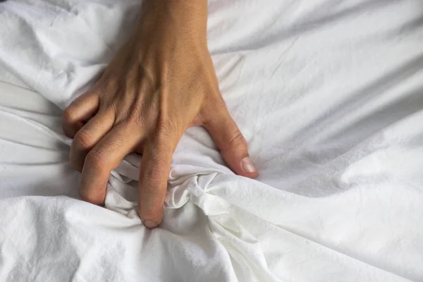 Close up detail of a womens hand grabbing on to the bed sheets