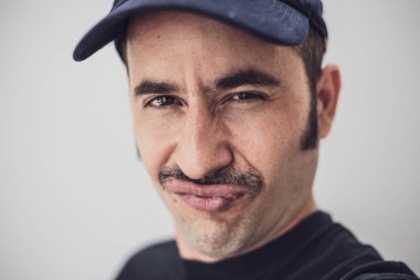 Belirgin bir bıyık ve sorunsuz bir arka plan karşı bir şapka ile beyaz erkek yaramaz bir görünüm ile kameraya bakar
