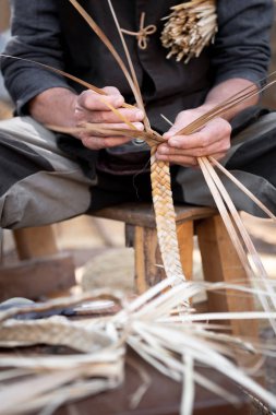 Yaşlı hasır ustası, elleri izole edilmiş ön grupta çalışıyor.