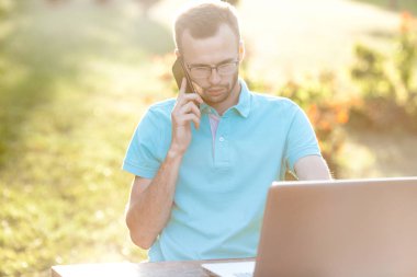 Gözlüklü genç iş adamı telefon kullanır. Serbest çalışma açık havada