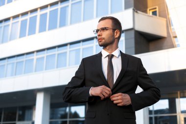 Resmi siyah elbiseli genç işadamı Cam ofis binası önünde duruyor. İş portre