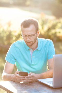 Gözlüklü genç iş adamı telefon kullanır. Serbest çalışma açık havada