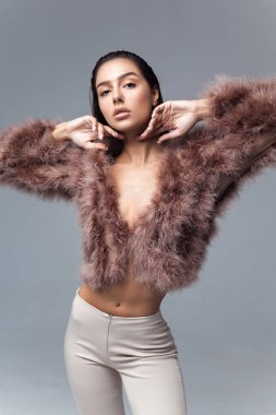 Tüylü, pembe pelerinli, yapay kürklü ve gri arka planda bej renkli pantolonu olan zarif bir kız. Moda retro tarzı