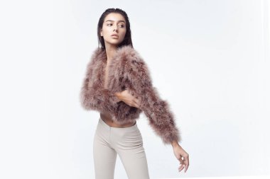 Tüylü, pembe pelerinli, yapay kürklü ve gri arka planda bej renkli pantolonu olan zarif bir kız. Moda retro tarzı