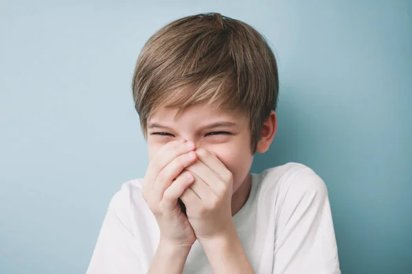 Laughing boy covers his mouth with his hands. Emotion concept