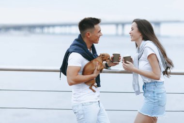 Deniz promenade üzerinde küçük köpek ile genç mutlu çift yürüyüş. Yaşam tarzı kavramı