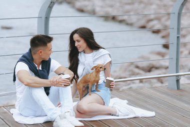 Deniz promenade üzerinde küçük köpek ile genç mutlu çift yürüyüş. Yaşam tarzı kavramı