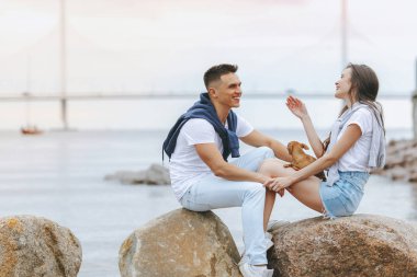 Genç mutlu çift deniz bay yakınındaki taş üzerinde otururken gülüyor. Yaşam tarzı kavramı