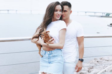 Deniz promenade üzerinde küçük köpek ile genç mutlu çift yürüyüş. Yaşam tarzı kavramı
