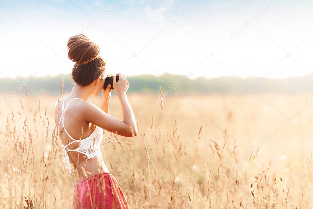 Young attractive girl with camera in field at sunset. Outdoors romantic concept