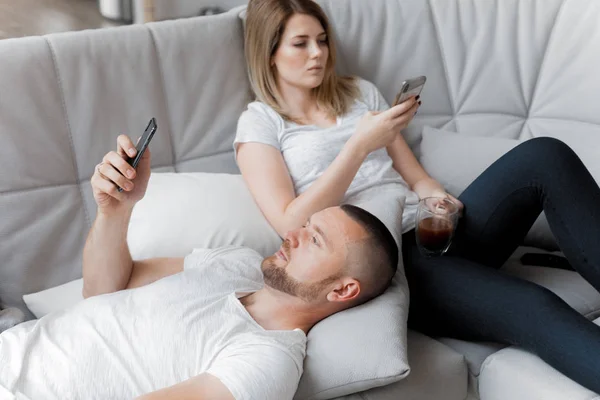 Young couple uses phones on sofa at home. Family relaxation lifestyle