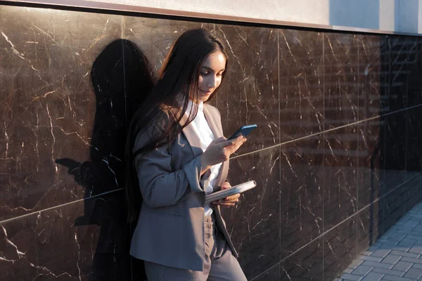 Young attractive girl in business suit uses phone. Lifestyle and business portrait
