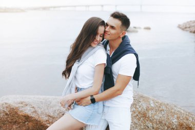 Deniz tarafından taş üzerinde oturan genç güzel pozitif çift. Yaşam tarzı kavramı