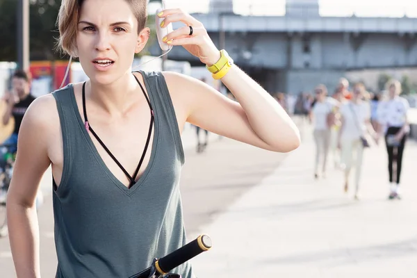 Young slim woman with short haircut on bicycle with headphones. Lifestyle and activity in city. Emotional portrait