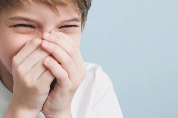 Laughing boy covers his mouth with his hands. Emotion concept