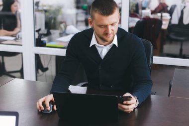 Sakin ciddi genç adam ofis masasında çalışırken telefon kullanır. İş portre