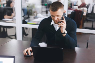 Sakin ciddi genç adam ofis masasında çalışırken telefon kullanır. İş portre