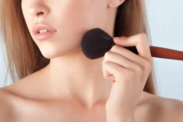 Young beautiful girl with brush for powder close-up. Cosmetics and care for young skin. Anonymous portrait