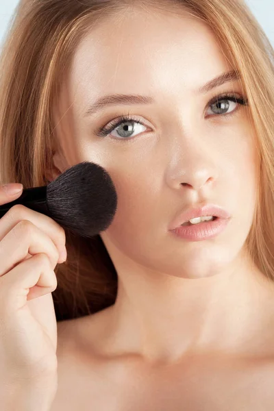 Young beautiful girl with brush for powder close-up. Cosmetics and care for young skin
