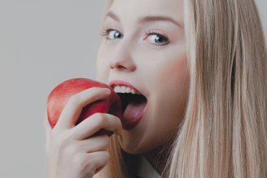 Genç oyuncu tatlı bir sarışın kırmızı elma yiyor. Duygular, gıda, diyet ve yaşam tarzı
