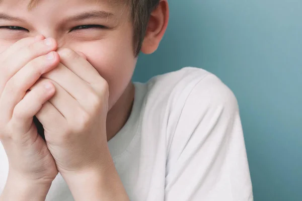 Laughing boy covers his mouth with his hands. Emotion portrait