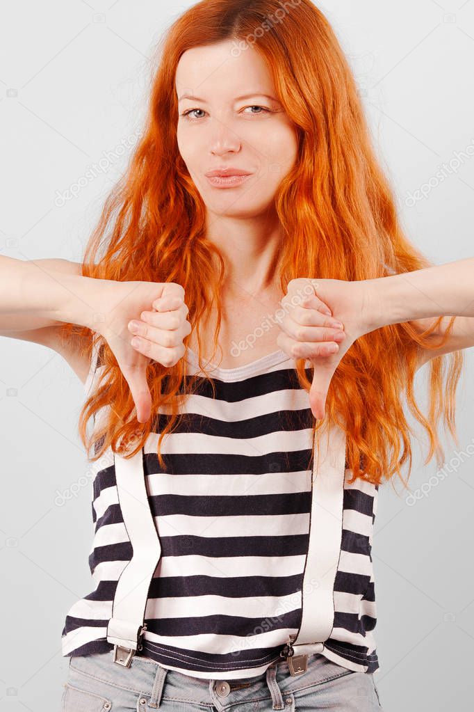 Redhead girl frowns, squints and shows thumb down. Negative and Condemnation