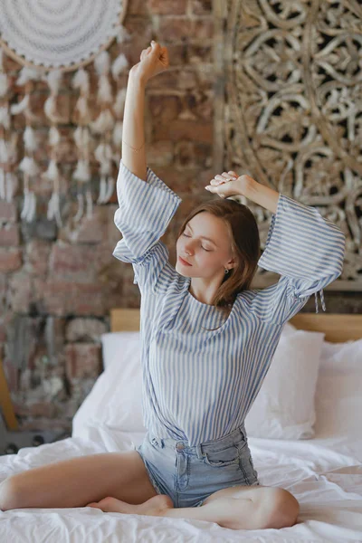 Jong lief meisje zit op bed en strekt haar armen omhoog — Stockfoto