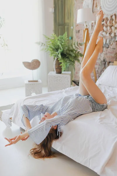 Giovane dolce ragazza è sdraiata sul letto con le gambe sollevate — Foto Stock