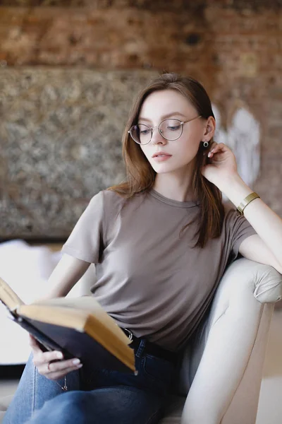 Молодая милая девушка в очках сидит и читает книгу — стоковое фото