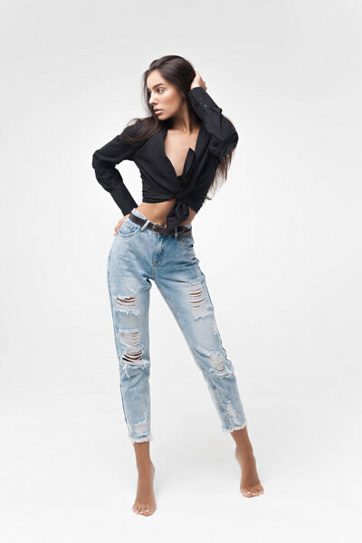 Молодая крутая хипстерша в черной рубашке и синих банановых джинсах стоит на белом фоне. Модный современный стиль
