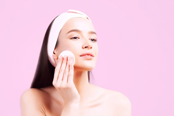 Young beautiful woman with perfect skin cleans skin with cotton pads on pink background. Skin care and age cosmetics concept