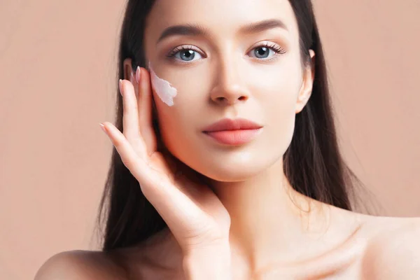 Young beautiful woman apply cream on clean perfect skin. Skin care and age cosmetics concept