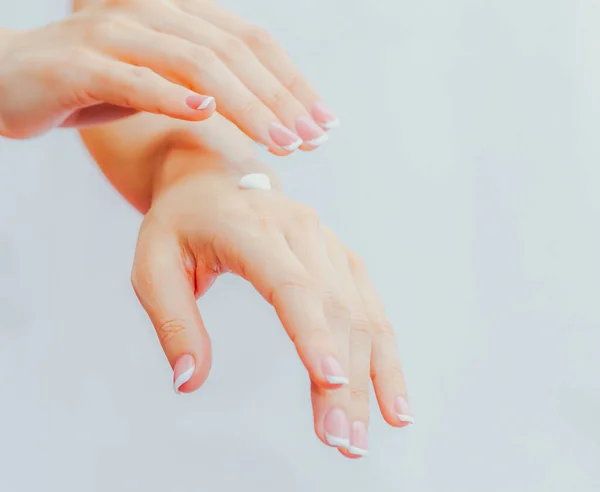 Woman with french manicure applies cream to her hands. Hand skin care and massage. Hands close up