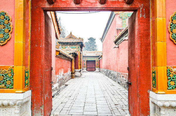 The gate door of red wall of Forbidden Palace with stone walking path between 2 buildings or house.