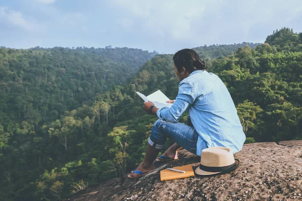 Hombre asiático viajar relajarse en las vacaciones. asientos relajarse leer libros sobre acantilados rocosos . — Foto de Stock