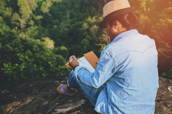 Asiatische Männer reisen entspannt in den Urlaub. Sitzgelegenheiten entspannen beim Lesen von Büchern auf felsigen Klippen. — Stockfoto