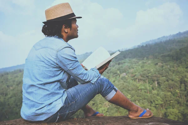 Asiatische Männer reisen entspannt in den Urlaub. Sitzgelegenheiten entspannen beim Lesen von Büchern auf felsigen Klippen. — Stockfoto