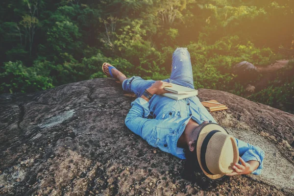 Viagem homem asiático relaxar no feriado. assentos relaxar ler livros em penhascos rochosos . — Fotografia de Stock