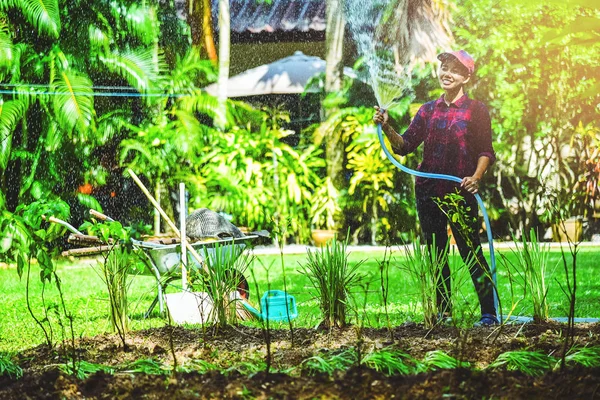 Asian women use hose garden watering the vegetable garden.