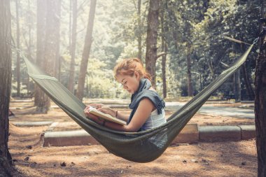 Oturmuş kitap okuyan kadınlar. Hamakta. Parktaki doğal atmosferde
