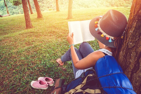 Las mujeres asiáticas se relajan en las vacaciones. Siéntate a leer libros sobre pastizales en el parque. educación, leer un libro, libro, Escribir una nota, diario, naturaleza, al aire libre, vacaciones, deporte, ejercicio, relajarse, viajar Tailandia, verano . — Foto de Stock