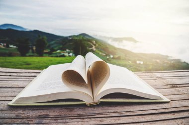 Kitap ahşap bir balkonda duruyor. Dağ manzarası, dağ köyü, kalp şeklini kapat kağıt, aşk hikayesi, mutlu sevgililer günü konsepti