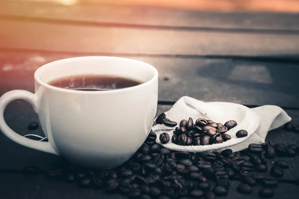 Café quente é em uma xícara branca Coloque no chão de madeira com grãos de café — Fotografia de Stock