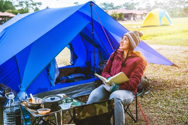 As mulheres asiáticas viajam relaxar nas férias. acampar na Montanha. Sente-se escreva um bilhete na cadeira. Acampamento turístico durante a noite na montanha. barraca de acampamento, camping Tailândia, educação, ler um livro, livro, diário. viagem Tailândia . — Fotografia de Stock