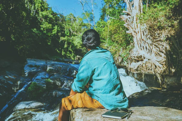 Asijský muž cestuje přírodou. Cestování je v klidu. Studie četla knihu. Příroda výuka napište si poznámku v vodopádu použijte léto. V Thajsku — Stock fotografie