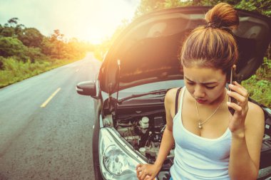 Asyalı kadınlar araba yol kırık. Kaputu aç, motoru kontrol et. Genç kadınlar seyahat ediyor, araba kullanıyor, seyahat ediyor, ortada arabaları boşa harcıyor. Arabayı tamir etmek için bir teknisyeni aramak için telefonu kullanıyor..