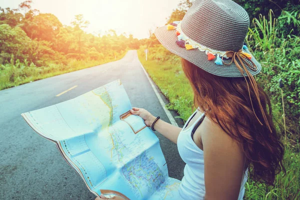 アジアの女性は休日にリラックス旅行します。自然の真ん中にある田舎道の地図を見てください。その少女は地図旅行を読むために勉強していた。道路、交通ルート、農村道路、夏、自然、屋外、休日、リラックス、旅行タイ. — ストック写真