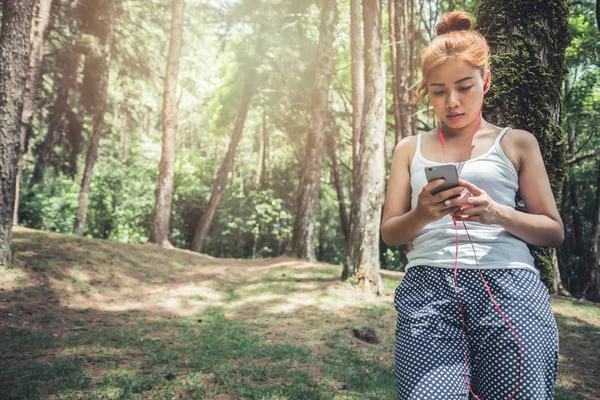 Women listen to music Relax in the nature park. The girl who is sitting and relaxing under the pine tree.