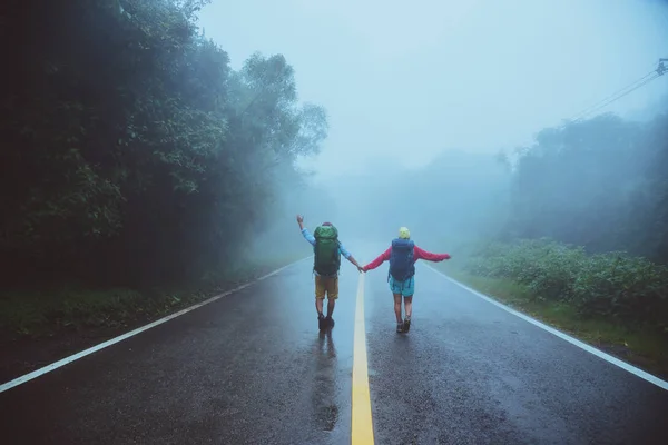 Lover Asian man and Asian women travel nature. Walk on the road route. traveling nature happily. Amid the mist rainy. in the rainy season. — Stock Photo, Image